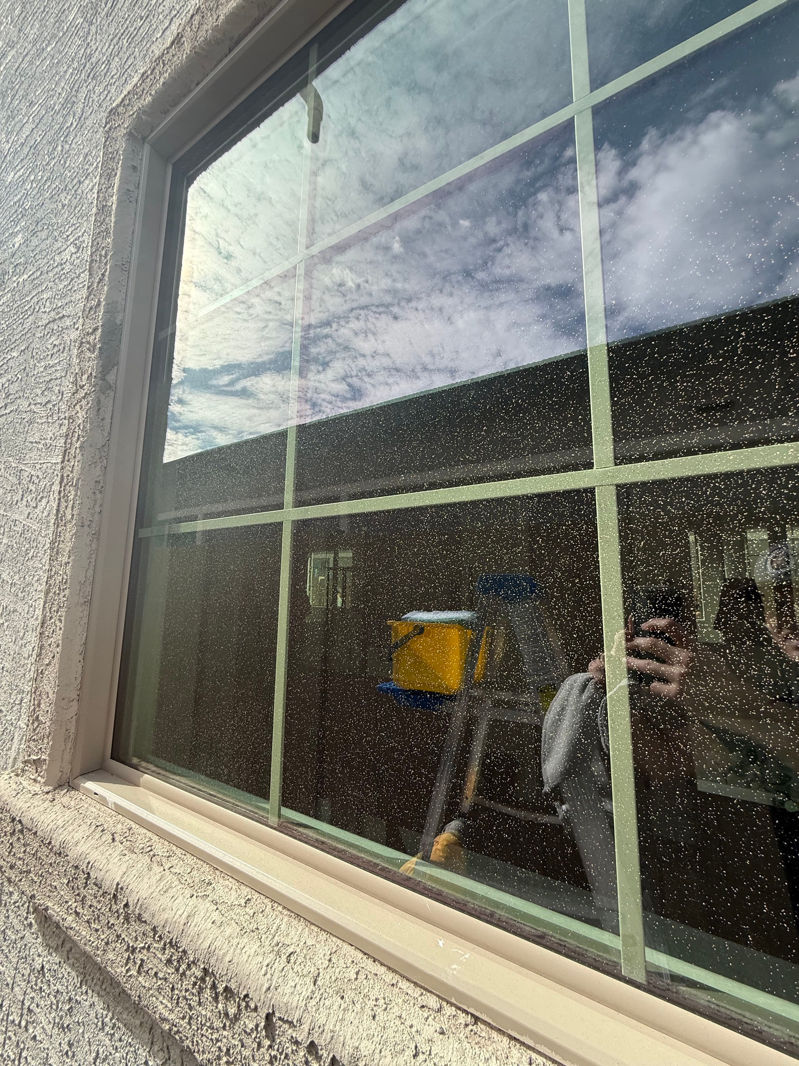 Reflection of clouds in a window with a ladder and cleaning supplies visible.