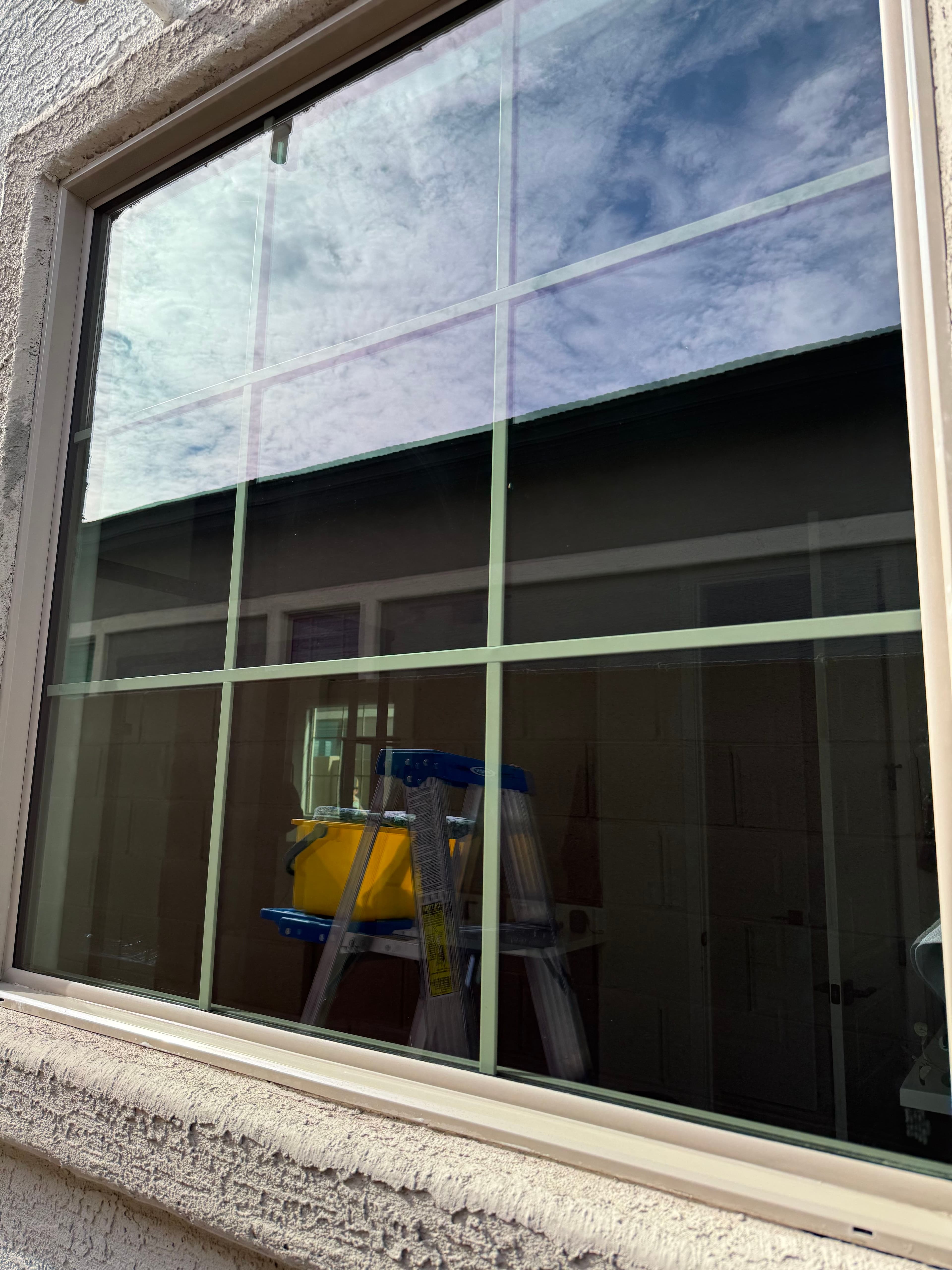 Window reflecting sky with ladder and bucket visible outside.