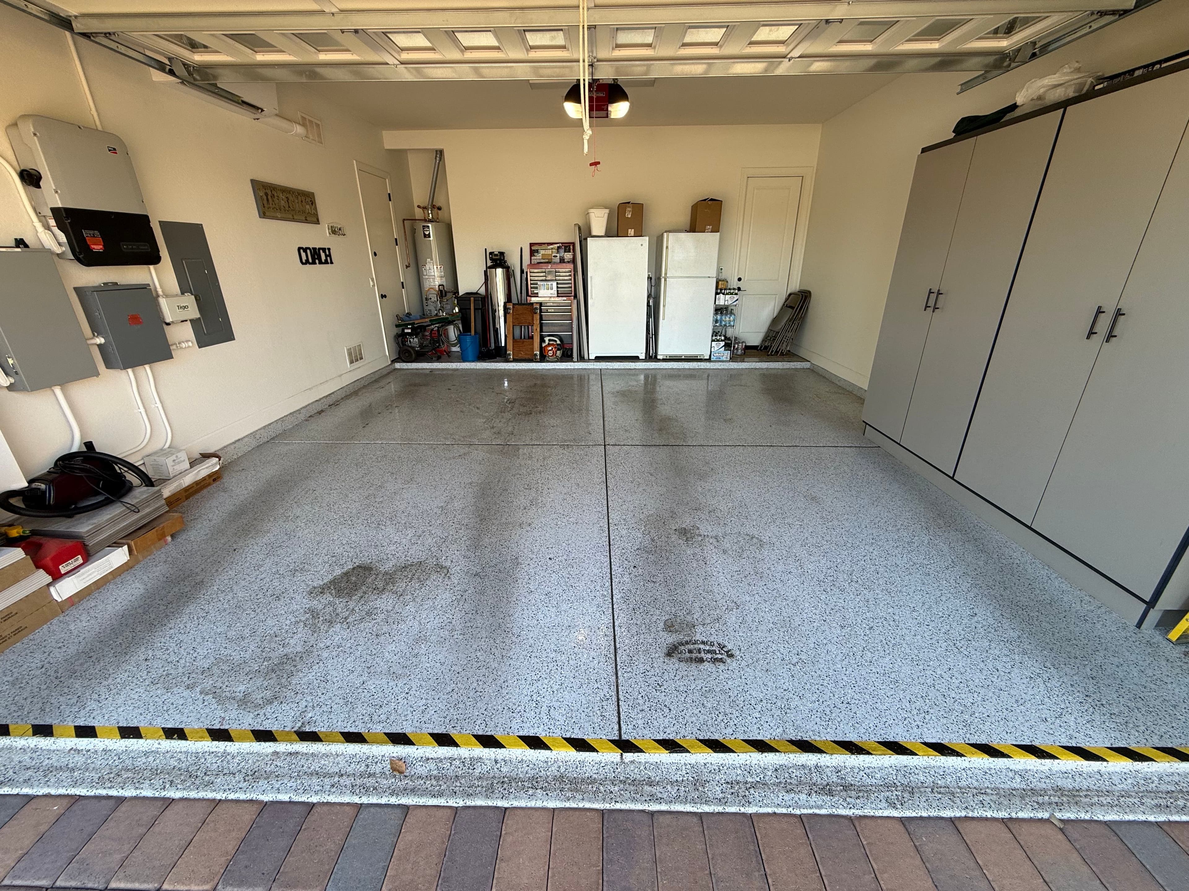 Clean garage with epoxy floor, storage cabinets, and appliances against the wall.
