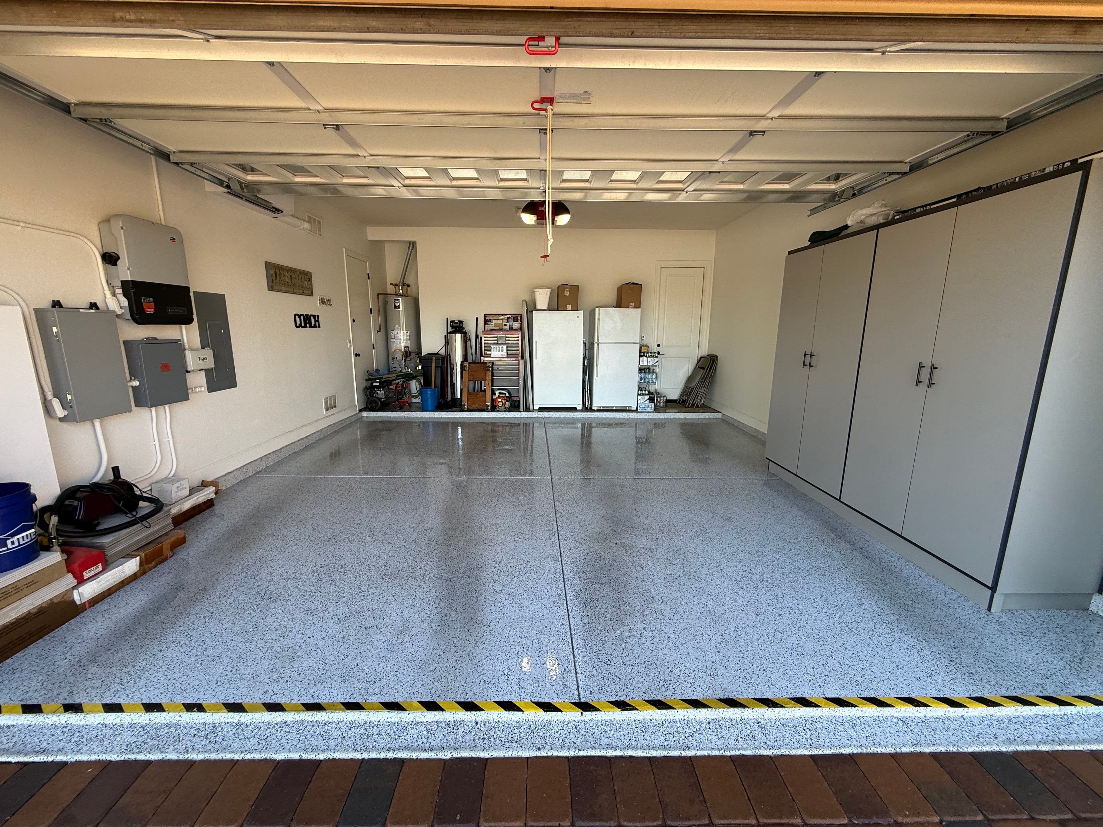 Clean and organized garage with epoxy flooring, cabinets, and tools neatly stored.